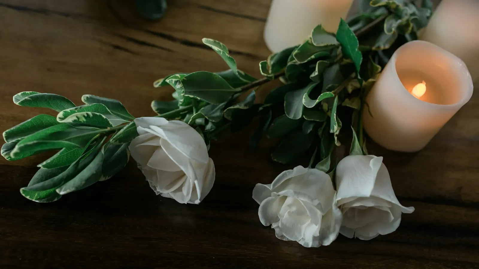 Weiße Rosen und Kerzen auf dunklem Holz