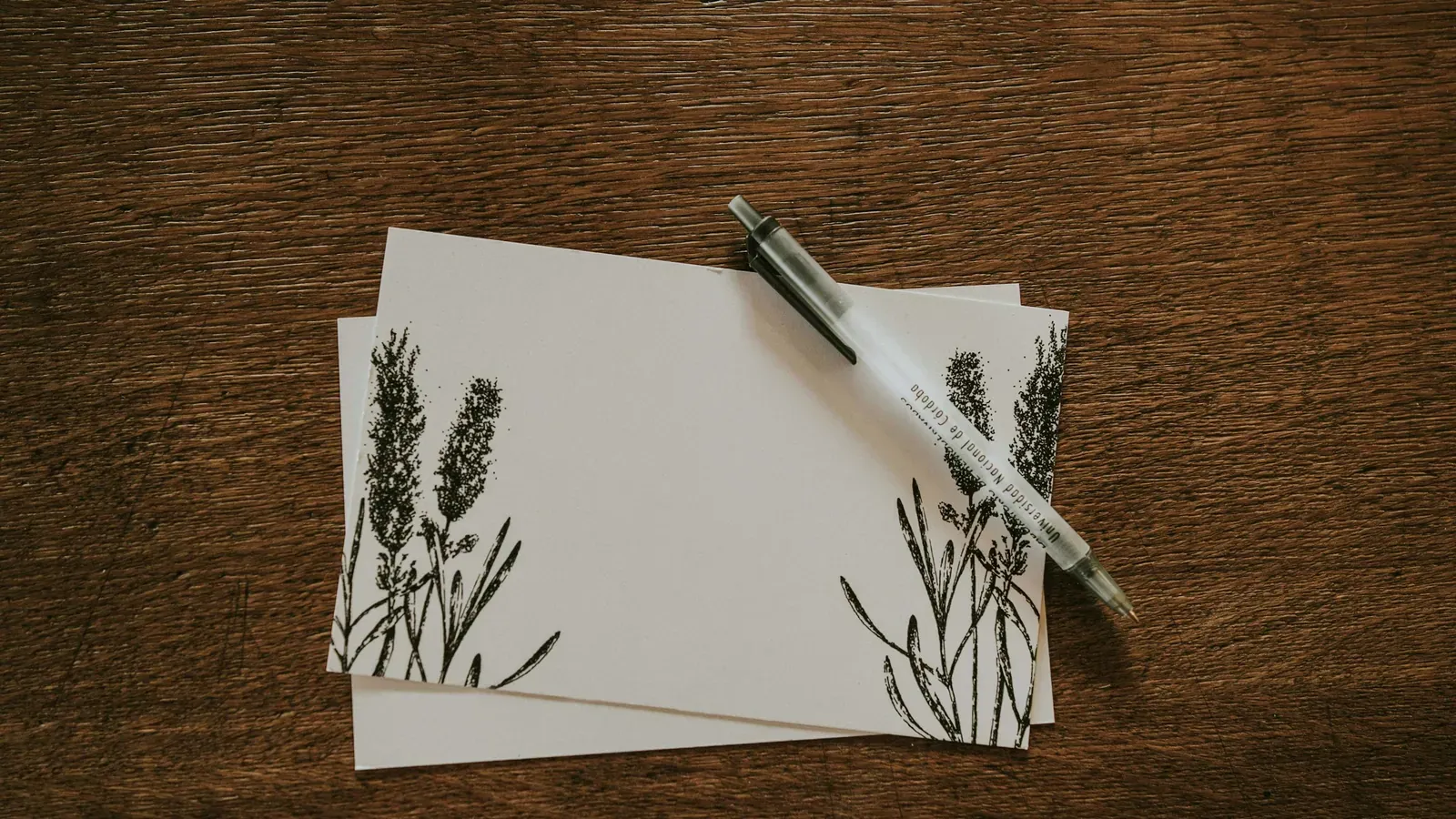 Karten mit botanischem Motiv und ein Stift auf einem dunklen Holztisch